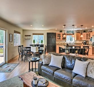 Open-concept living area at Moose Creek Lodge with leather sofa, full kitchen, and forest-view.