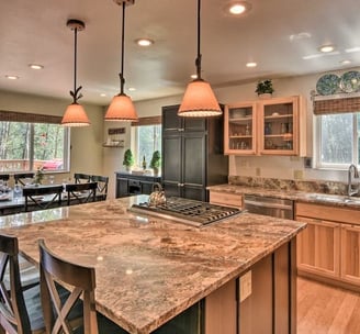 Spacious kitchen with center island, pendant lighting, and dining area overlooking forest views.