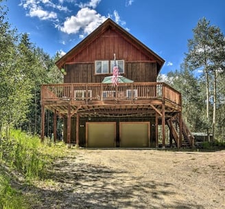 Rustic mountain cabin with a large elevated deck and two-car garage, surrounded by aspen trees.