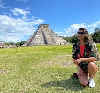 mulher de joelho em frente a pirâmide Chichén Itzá no méxico