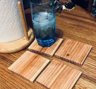 a glass of water on a square wooden cedar coaster sitting on a table