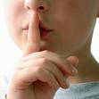 Haut d'un visage en partie caché avec index vertical sur la bouche pour dire : chut