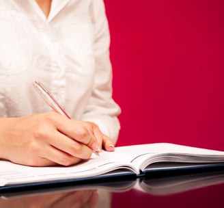 a woman is writing on a notebook with a pen and a pen
