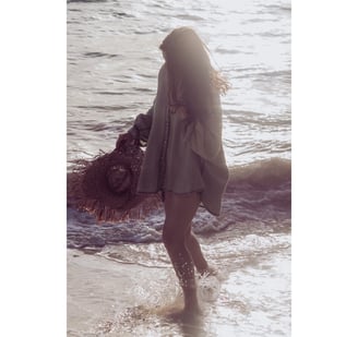 a woman walking on the beach with a hat