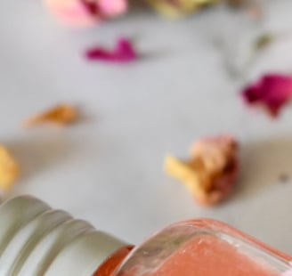 flacon de serum rose posé sur une table en marbre avec des pétales de rose