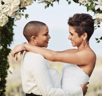 a lesbian couple at their wedding celebration under the arbour / bower dress in white 