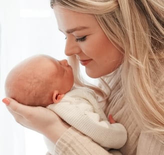 Newborn baby sleeping in mother’s arms, neutral tones, natural light