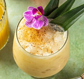 overhead shot of a beachy orange cocktail with flowery island garnishes