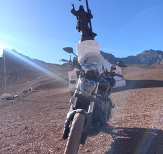 a motorcycle parked in a desert area with a statue of jesus on the side of Cristo Redentor Andes