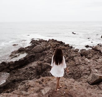a woman in a white dress standing on a rocky beach