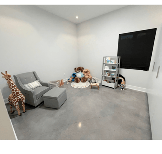 Minimalist kids’ playroom with reading corner, stuffed animals, and gray armchair.