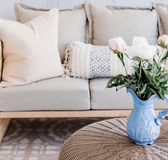 Soft neutral living room with elegant cushions and floral accent in blue vase.