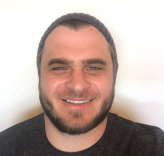 Keith Enterante wears a black shirt and beanie, smiling at the camera in front of a white wall.