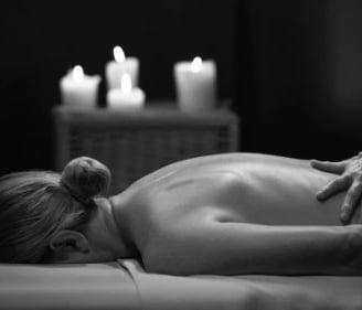Woman lying on her front enjoying a massage, there are candles glowing in the background
