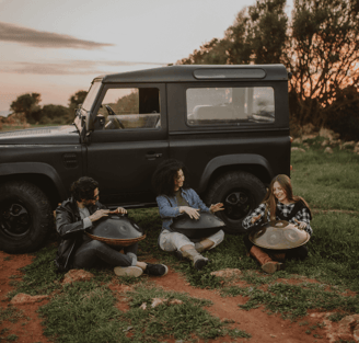 Three musICIAn playing Sew Handpan on the nature close to a jeep