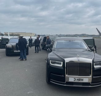 a rolls royce black car parked in front of a plane