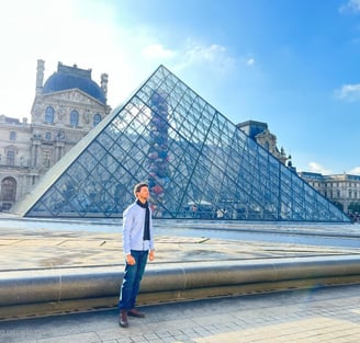 homem em pé em frente a parte externa do museu do Louvre em Paris
