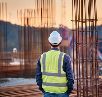 Ein Mann in einer Sicherheitsweste steht vor einer Baustelle mit Eisenflechterei