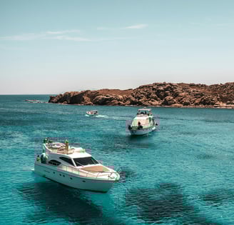 Boats floating on clear blue sea near rocky coast.