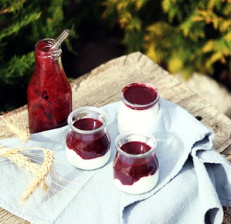 3 pots of yoghurt and berry topping outside with pine trees