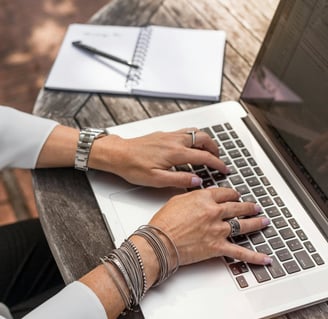 Frau tippt auf einen Laptop an einem Tisch draußen. Homeoffice und Karriere