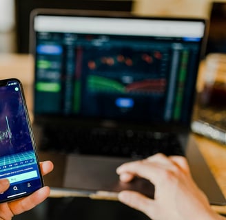 Pessoa analisando gráficos financeiros em um smartphone e um notebook