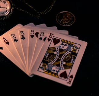 A spread hand of playing cards, witha pocketwatch, coin, chain and candlestick on the same surface in the background.