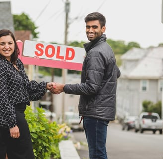 First Time home Buyer in Clagary. A man and woman shaking hands in front of a sold sign