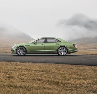 a green bentley driving down a road with a mountain in the background