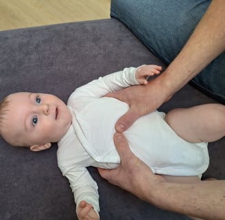 een baby ligt op een tafel met 2 handen van een man