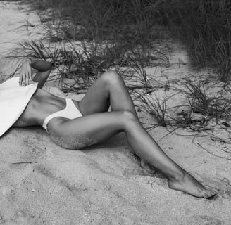 Black and white photo of a woman in a sunhat lounging on the beach