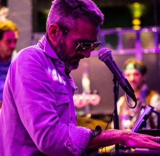 un homme joue du piano et chante lors d'un concert. Il est éclairé d'une lumière violette