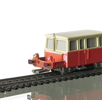 ancienne locomotive rouge et blanche de train miniature, sur rail, fond blanc avec reflet