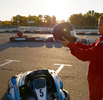 Jeune homme en combinaison rouge tenant un casque devant un karting sur une piste extérieure.