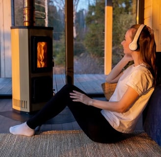 Estufa de pellets con fuego perfecta con mujer escuchando musica con cascos en el suelo de una casa