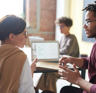 homem e mulher conversando em sala de aula com um notebook ao fundo