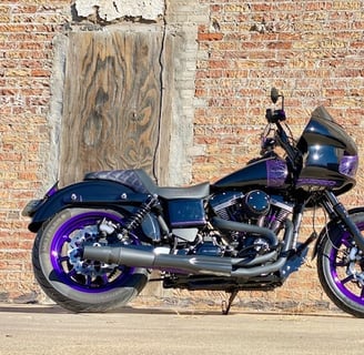 black motorcycle with purple pinstripping parked in front of a old brick wall