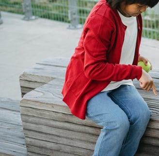 child holding a ball motioning for the dog beside her to lie down