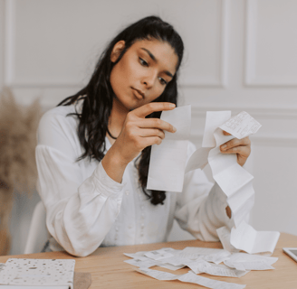 a woman is holding a piece of receipt with a pile of receipts and a notepad