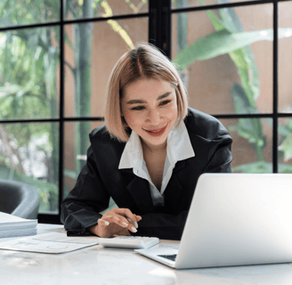 a blonde woman in a suit and tie is smiling and looking at her laptop using a calculator