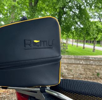 Rider departing on motorcycle with Remy helmet bag secured to the bike, framed against a glowing sun