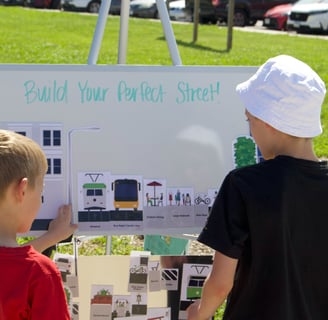 Two children at a whiteboard activity titled "Build Your Perfect Street!"