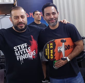 O vocalista da Banda CPM 22 em pé ao lado do ganhador, segurando o skates que ganhou da banda