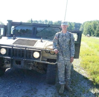 Tomkins in army uniform standing next to a green humvee covered in mud.