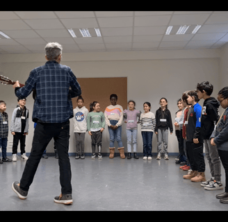 un musicien intervenant joue de la guitare en pleine séance musique avec des enfants dans une école