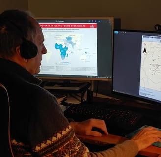 Photo of a man in front of two monitors with GEOINT maps displaying data on poverty and protests.