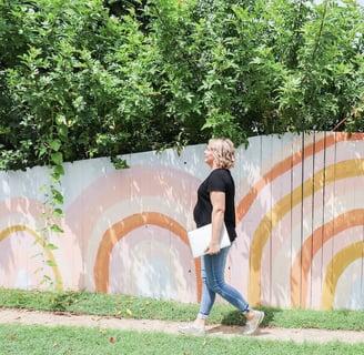 a woman walking down a sidewalk with a laptop in front of a wall