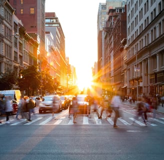 a busy city with traffic and pedestrians, and a bright sun setting in the background