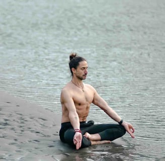 a man sitting on a beach with his hands on his knees, yoga position