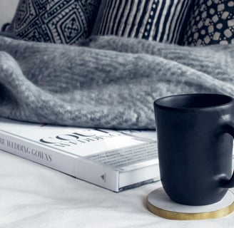 Black Ceramic Mug on Round White and Beige Coaster on White Textile Beside Book by  Isabelle Taylor 